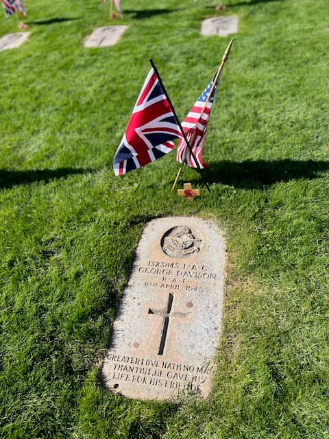 The flat granite headstone of LAC George Davison, RAF, who died 8th April 1943, marked with a Union Jack, a Stars and Stripes, and a poppy cross. The inscription reads: greater love hath no man than this, he gave his life for his friends.