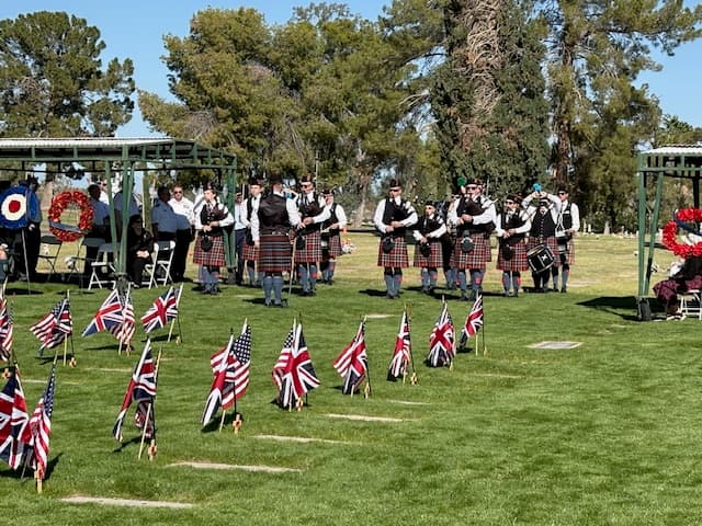 The Mesa Caledonia Pipe Band assembled on the cemetery green between rows of cadet headstones marked with British and American flags.