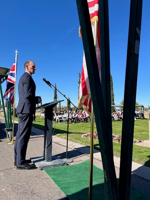 A speaker delivering remarks at the podium between the British and American flags.
